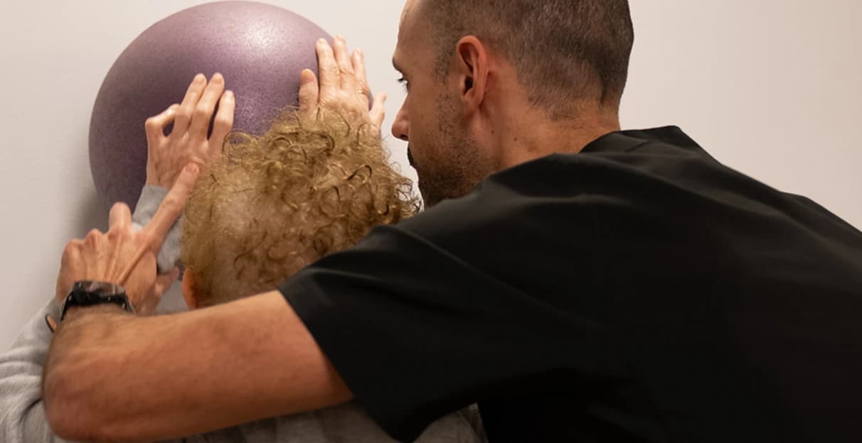Terapeuta guiando a una paciente en un ejercicio con pelota contra la pared.
